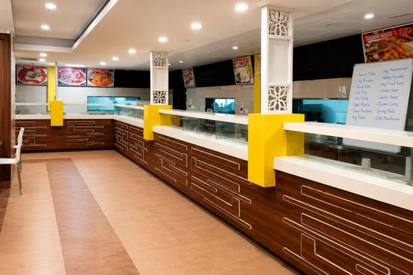 Inside a fast-food restaurant: long glass display counter with white top, dark brown panels, yellow supports, and menu boards on the walls.