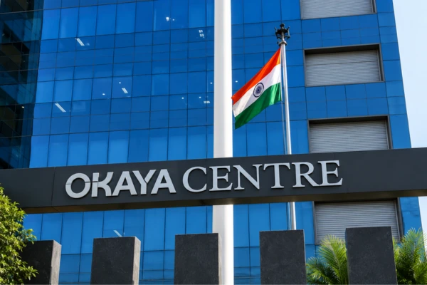 Blue glass office building with a flagpole bearing the Indian flag in front of a black Okaya Centre sign.